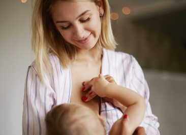 Back view of adorable six month old infant drinking breast milk. Attractive young European woman in home clothing cradling her baby daughter in arms, breastfeeding her, enjoying deep connection
