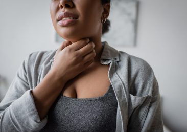 Cropped view of young multiracial woman touching sore throat at home