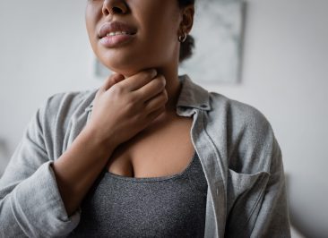 Cropped view of young multiracial woman touching sore throat at home