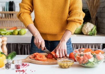 Healthy eating. Front view of female hands making salad cutting tomatoes in the kitchen