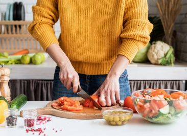 Healthy eating. Front view of female hands making salad cutting tomatoes in the kitchen