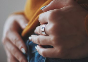 A vertical closeup shot of a female in an orange shirt wearing an expensive golden ring
