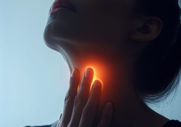 Woman in pain touching her neck due to a sore throat against a dark blue background, capturing the discomfort of throat inflammation from illnesses like laryngitis or tonsillitis